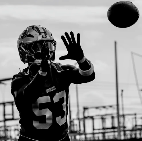 Jugador de los 49ers durante un entrenamiento, con infraestructura eléctrica al fondo.